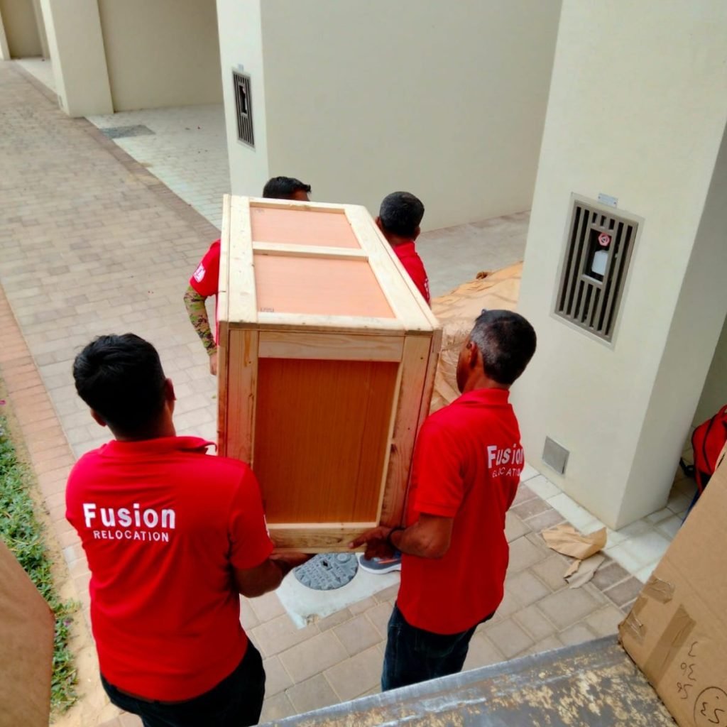 Four Fusion movers carrying a custom wooden crate through a Dubai compound