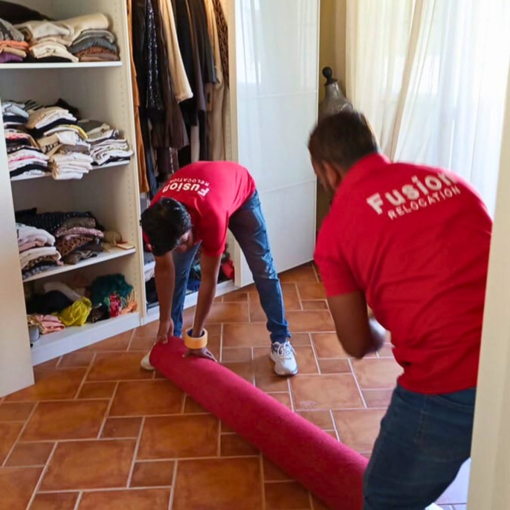 Fusion crew rolling a carpet in a Dubai walk-in wardrobe on packing day