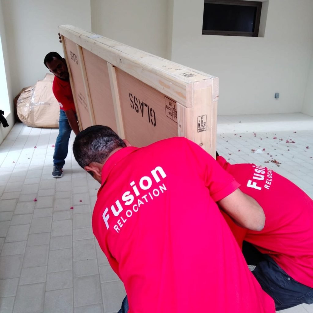 Fusion movers positioning a large GLASS-stencilled crate inside a new home