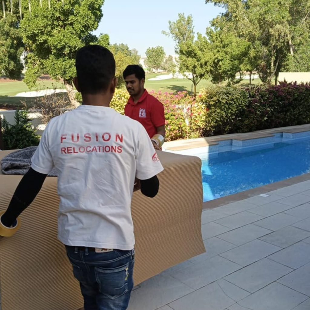 Fusion Relocations movers carrying packing materials past the pool of a Dubai villa